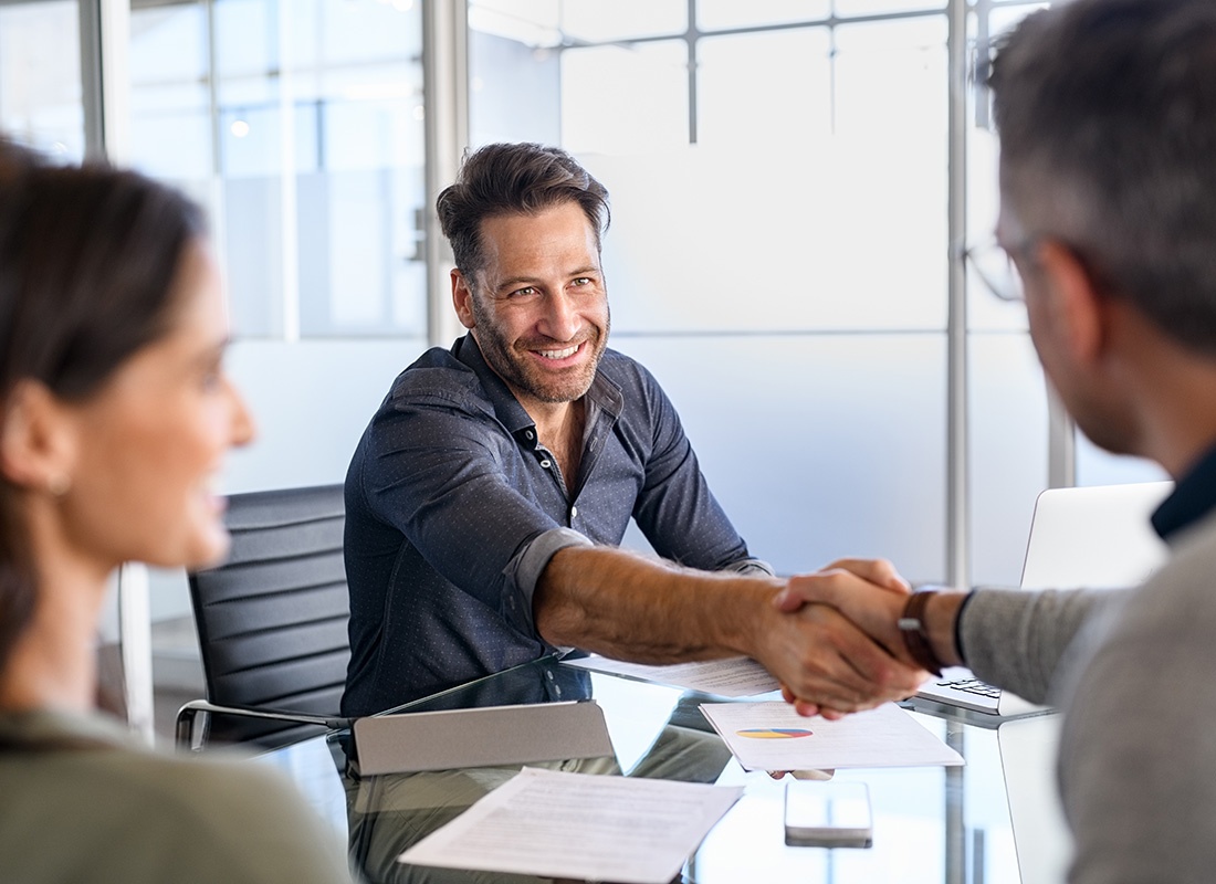 About Our Agency - Portrait of a Smiling Middle Aged Businessman Shaking Hands with his Clients Over a Glass Desk During a Meeting in the Office