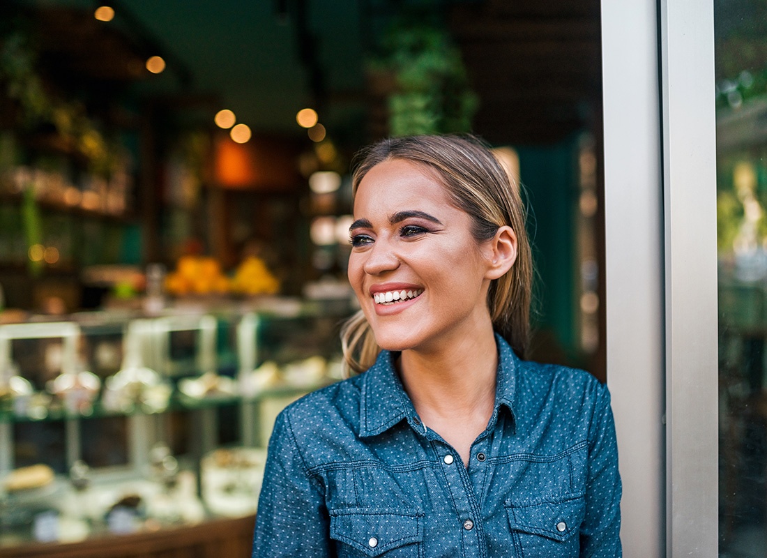 Business Insurance - Portrait of a Cheerful Young Female Business Owner Standing in the Front Door of her Main Street Store