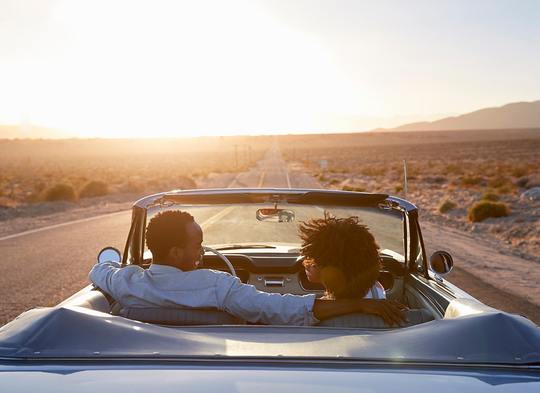 Personal Insurance - Back View of a Young Couple Looking at Each Other as They Drive Along a Country Road in a Convertible Through the Desert