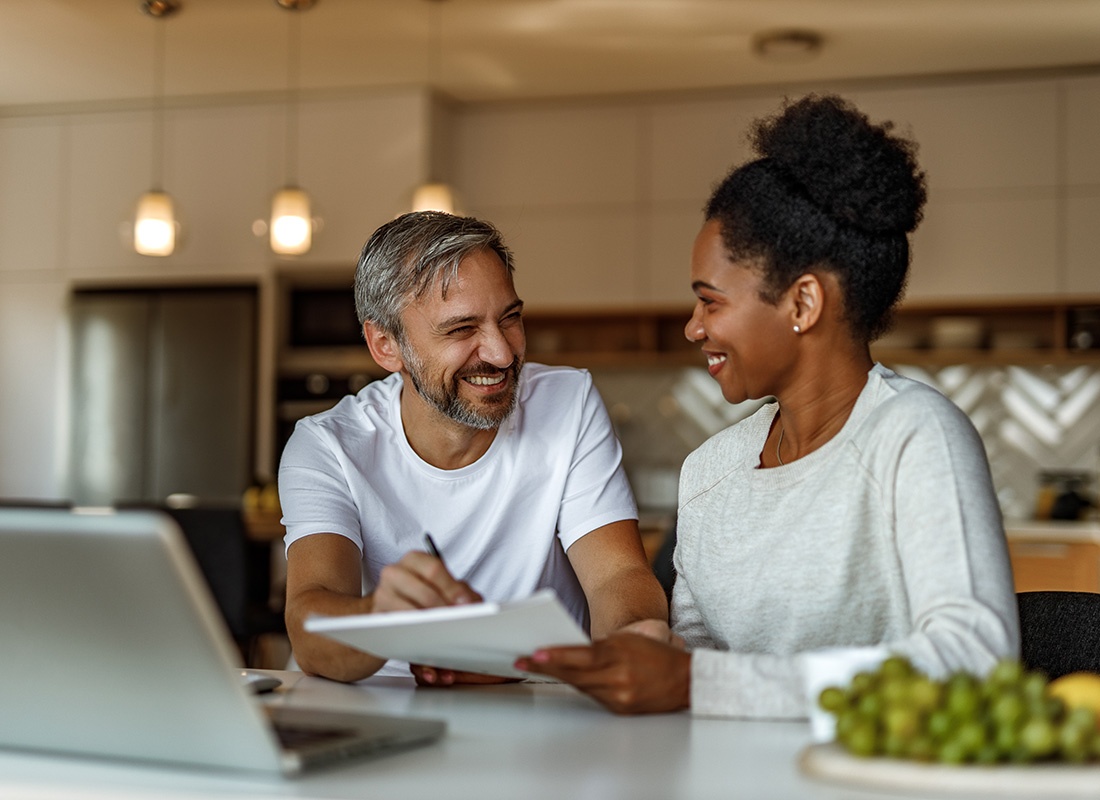 Read Our Reviews - View of a Cheerful Middle Aged Married Couple Spending Time Together Looking at Documents While Standing in the Kitchen with a Laptop on the Counter